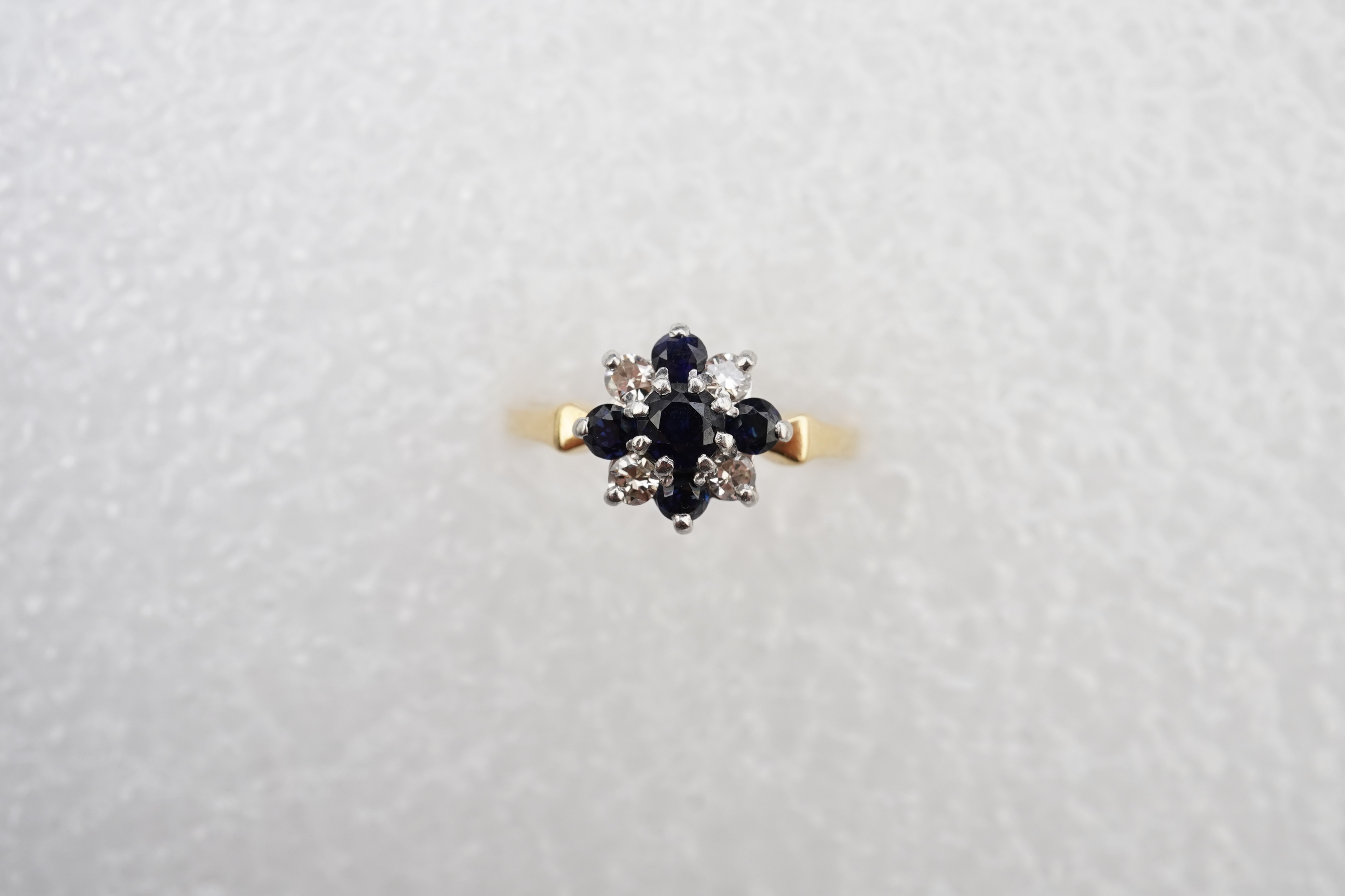 A sapphire and diamond cluster ring, set with circular-cut sapphires and brilliant-cut diamonds totalling approximately 0.20 carats, mounted in gold and platinum, size M, stamped 18CT PLAT, gross weight approximately 3.5